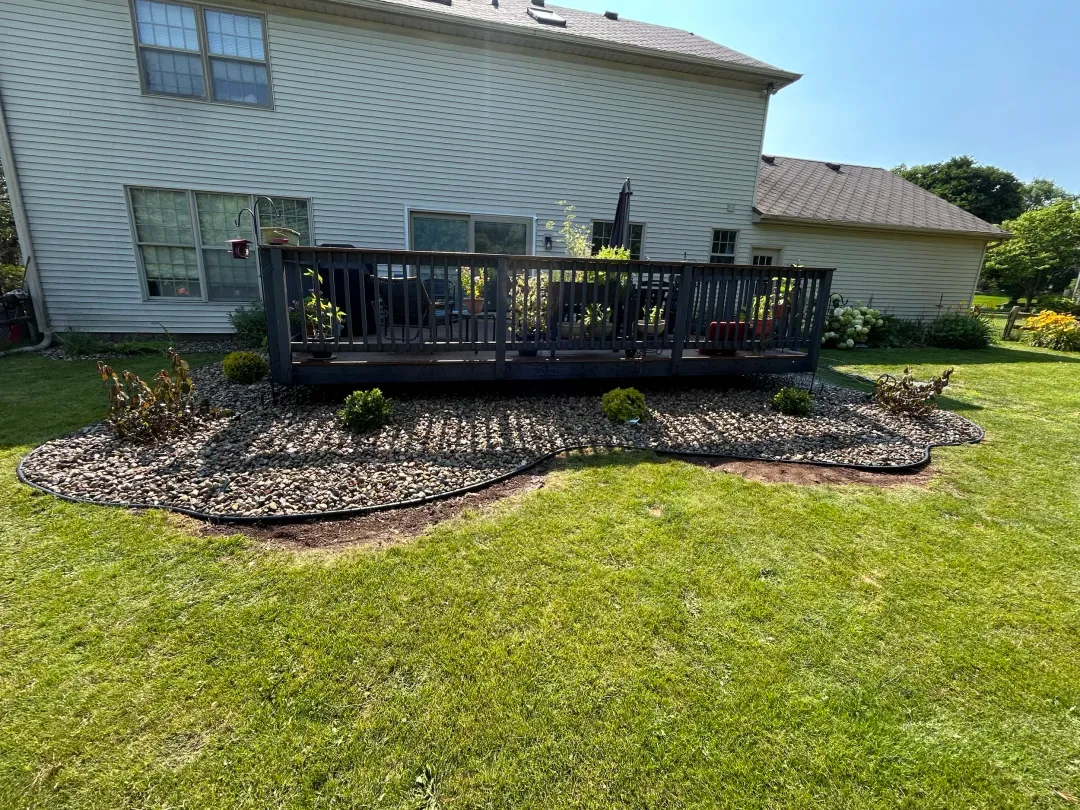 The same backyard deck with a curved stone bed and small, spaced shrubs
