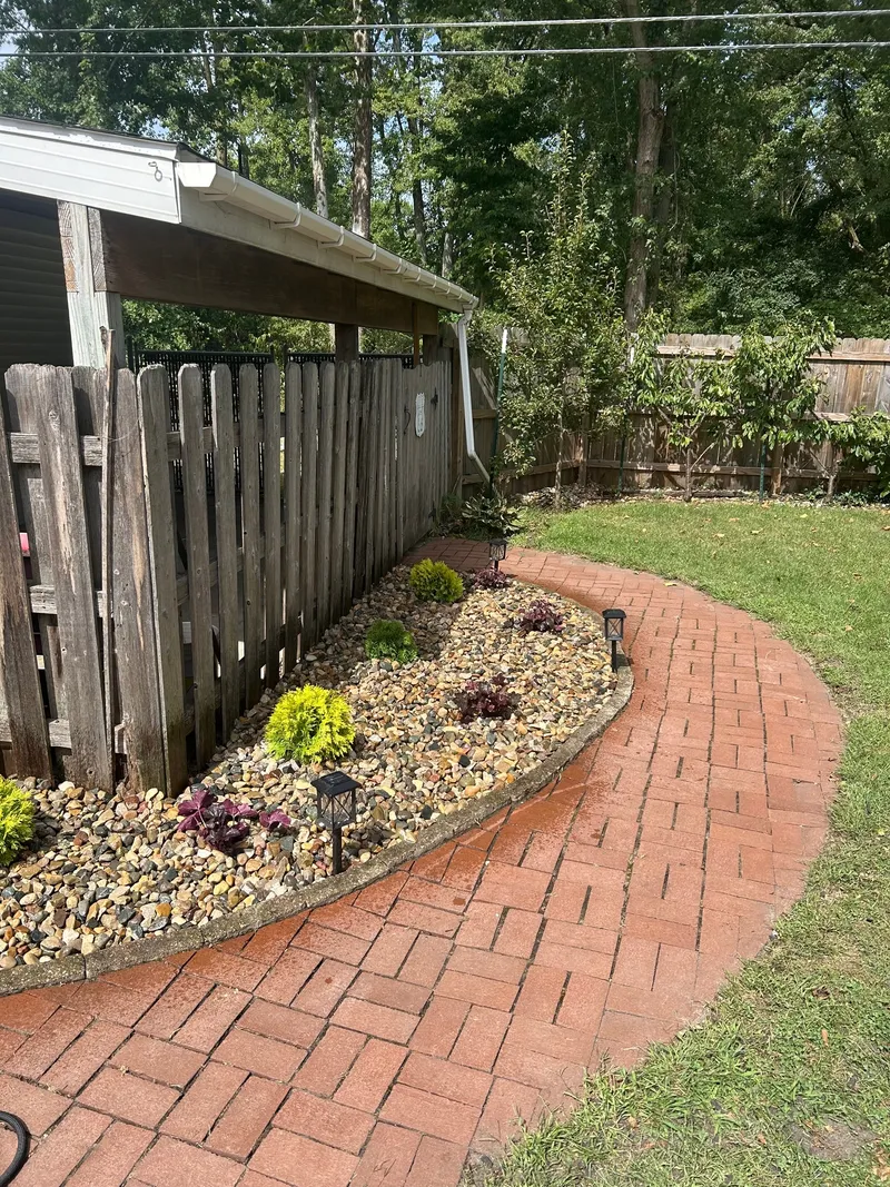 A refreshed stone bed and small plants beside a curved brick path