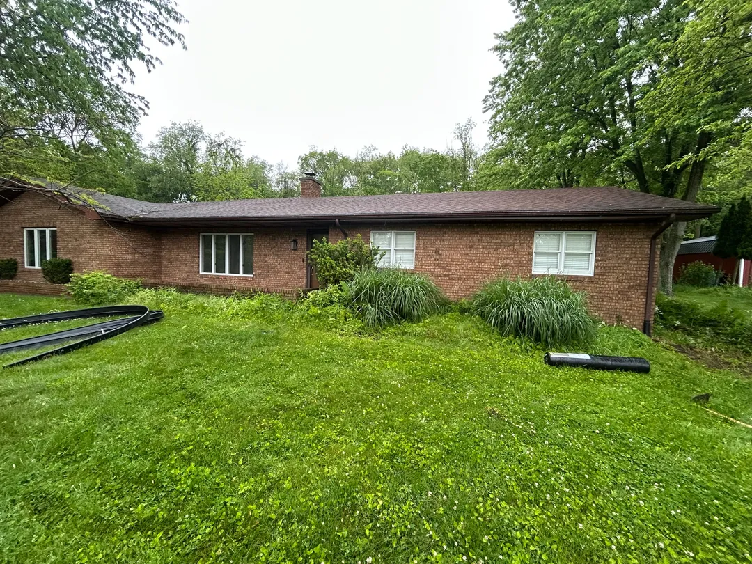 Overgrown beds along a single-story brick home