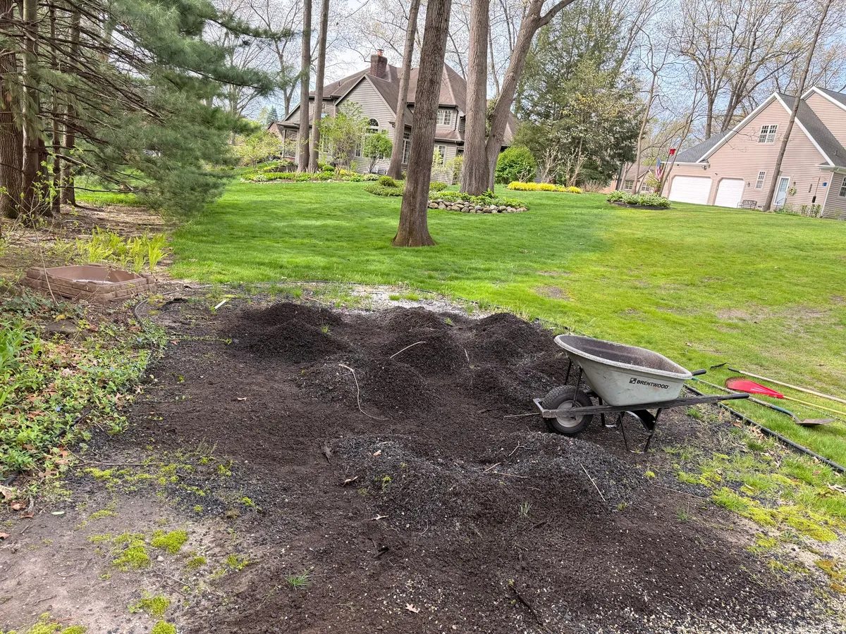 Loose soil, a wheelbarrow, and lawn tools beside an area being prepared