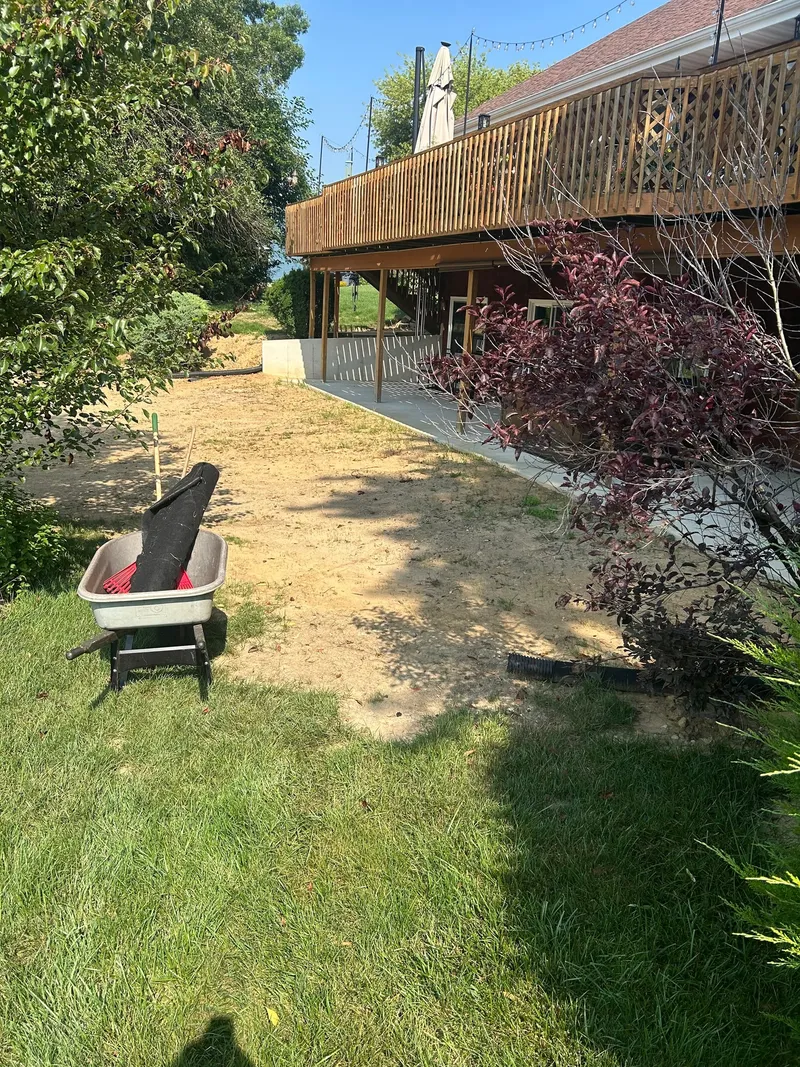 Straw-covered ground, stone edging, and a wheelbarrow beside a raised deck