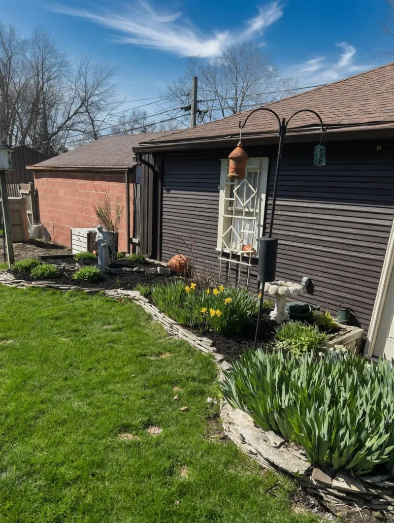 Spring flowers and green plants in a mulched bed beside an outbuilding