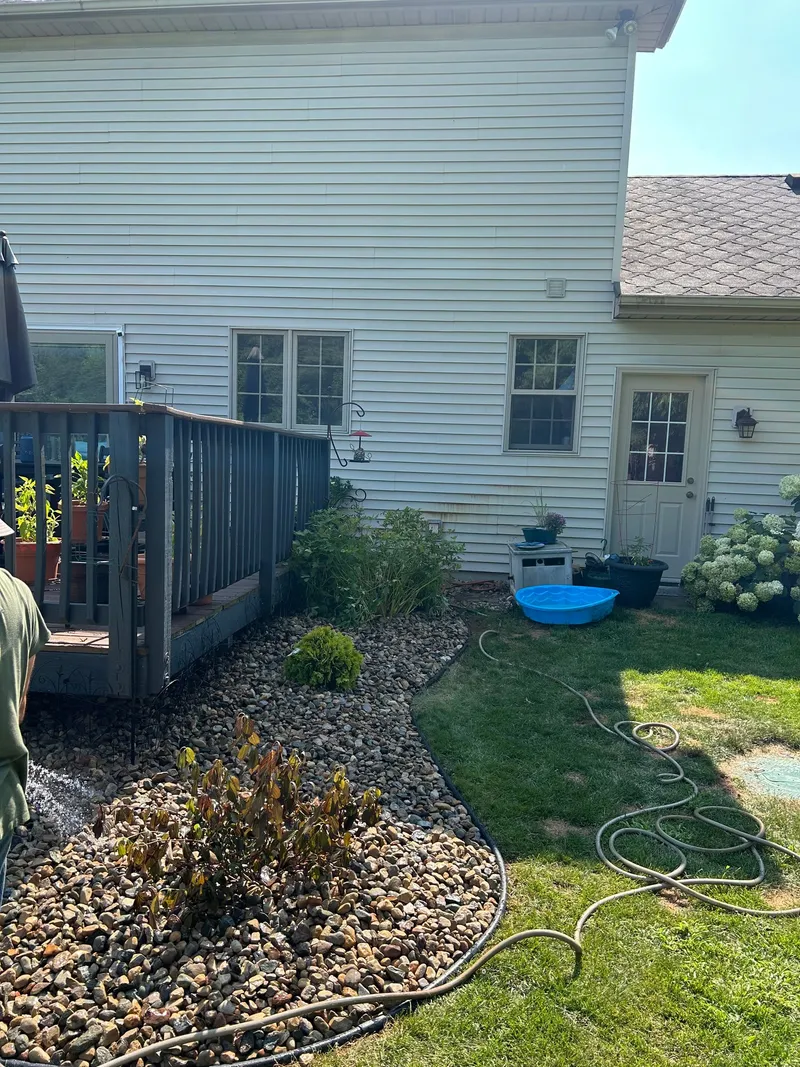 Small shrubs and stone beds beside house siding and a deck