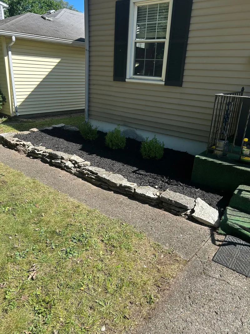 Small shrubs and fresh mulch beside a house entrance and stone edging