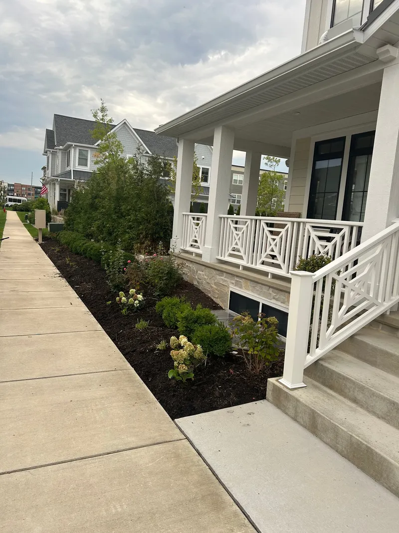 Plants beside a white front porch before the mulch refresh