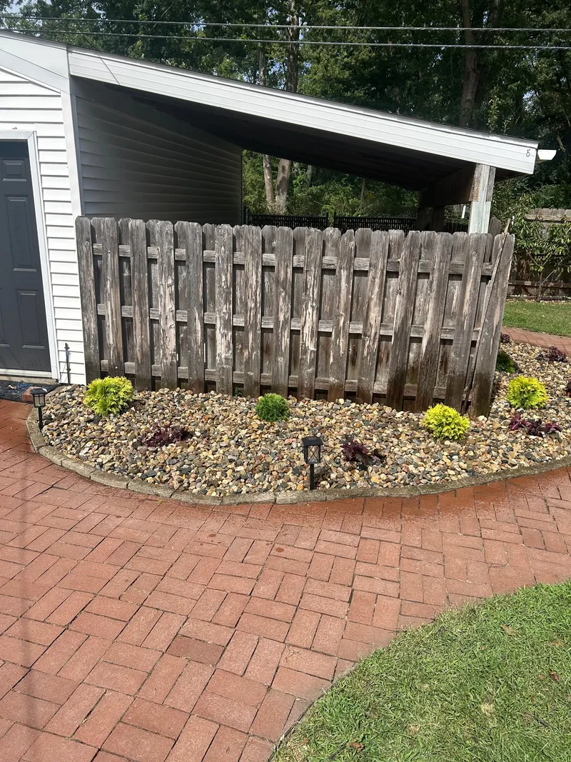 A curved stone bed with small plants below a wooden enclosure