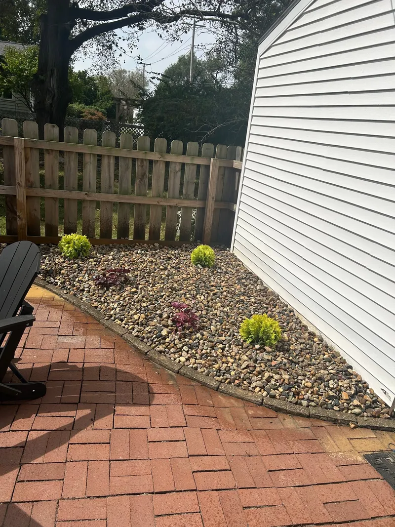 Fresh stone beds and shrubs between brick paving and a fence