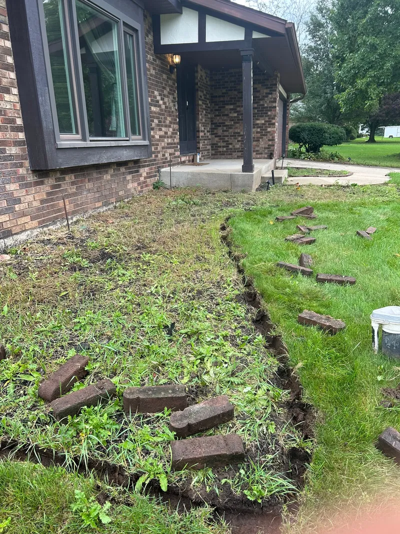Lifted edging and a dug border around a brick entryway during preparation