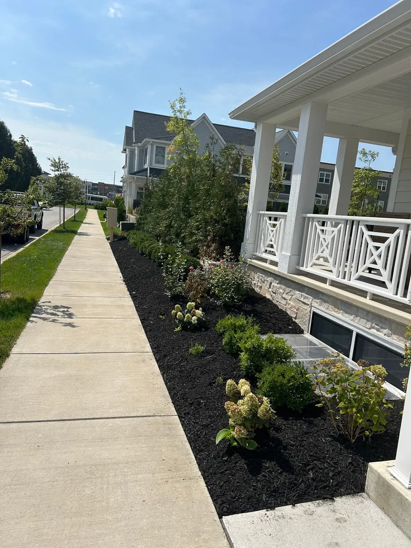 Fresh dark mulch and flowering plants along a white porch