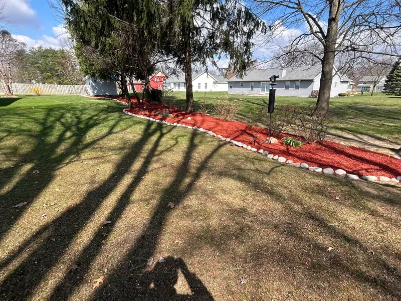 A long red mulch bed with stone edging beneath mature trees