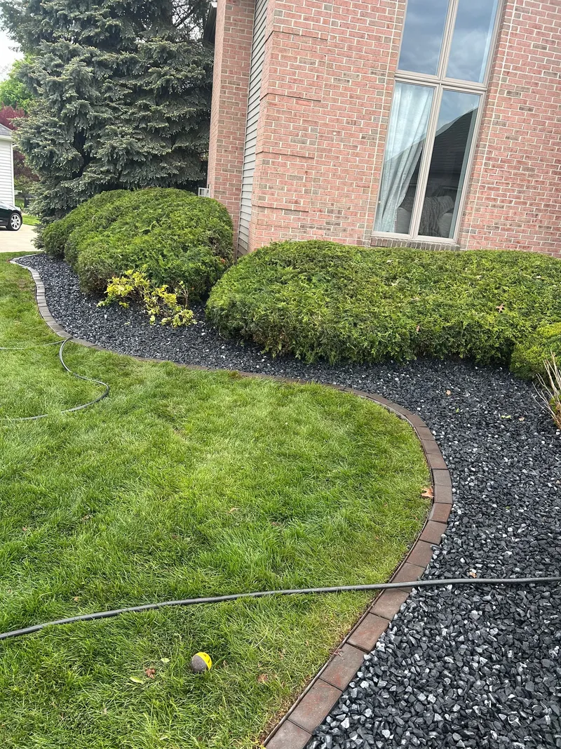 Trimmed shrubs and stone beds beside a brick home