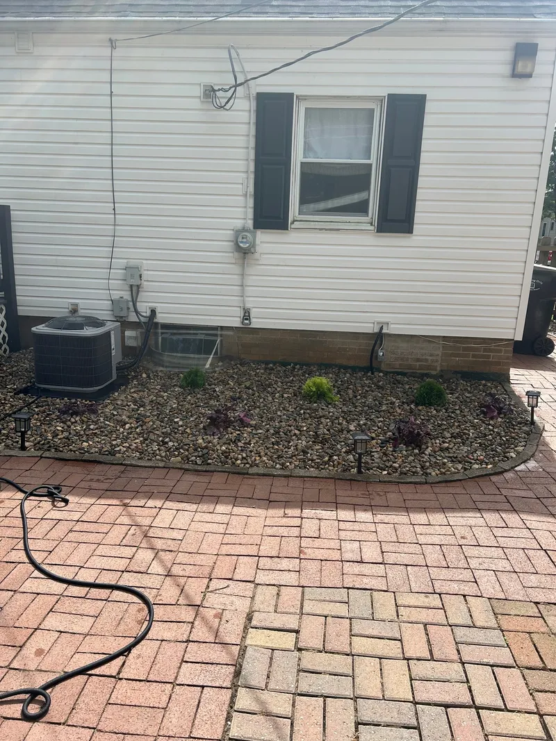 A curved stone bed and small shrubs below a house window
